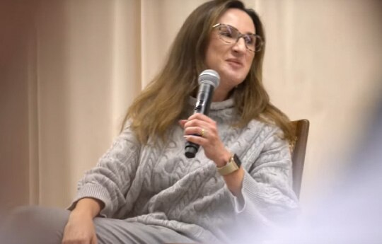 gestora do Itaú BBA com um microfone na mão, dando uima palestra