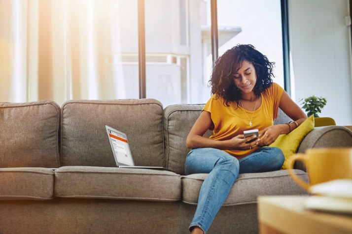 Cliente Itaú sentada no sofá acessando o app Itaú pelo celular 