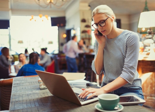 mulher consultando tabela geral de tarifas pelo computado e conversando com sua gerente de conta pelo celular.
