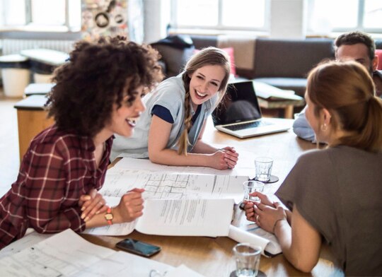 jovens reunidos com papéis e notebook sobre a mesa.