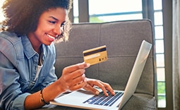 mulher com cartão na mão, sorrindo e olhando para o computador