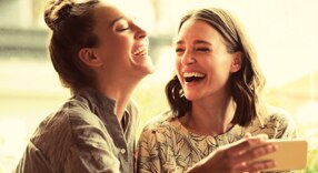 Amigas cartonistas Itaú Personnalité sorrindo enquanto observam algo no celular.