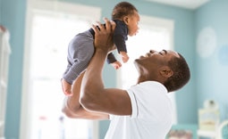 Pai, cliente Itaú Uniclass, segurando seu filho recém-nascido, após contratar um seguro familiar