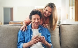 casal de clientes Itaú Uniclass, sentados no sofá, olhando para o celular para pedir um empréstimo