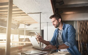 Jovem empresário trabalhando com celular e notebook em uma bancada