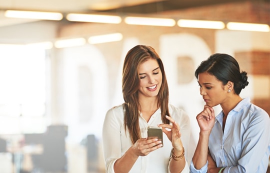 Mulher e gerente na agência conversando e sorrindo olhando o celular