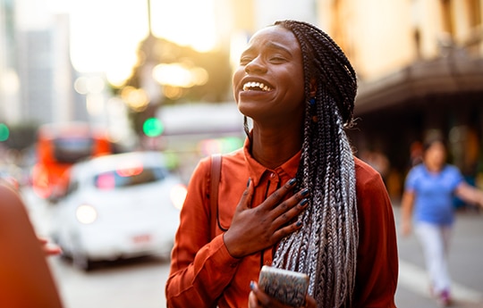 mulher segurando um celular com expressão de felicidade enquanto anda na rua