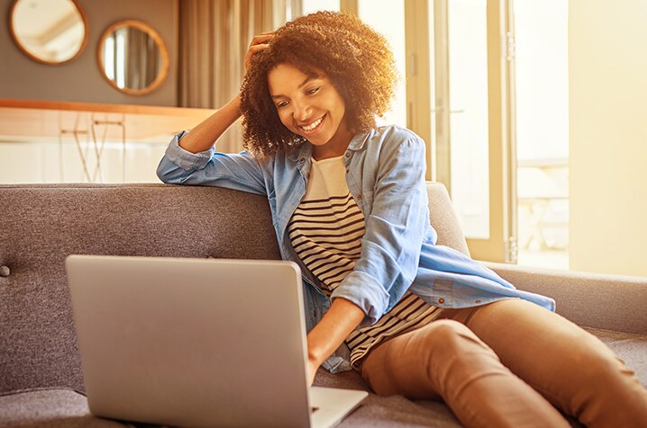 Cliente Itaú sorridente no sofá enquanto mexe no notebook.