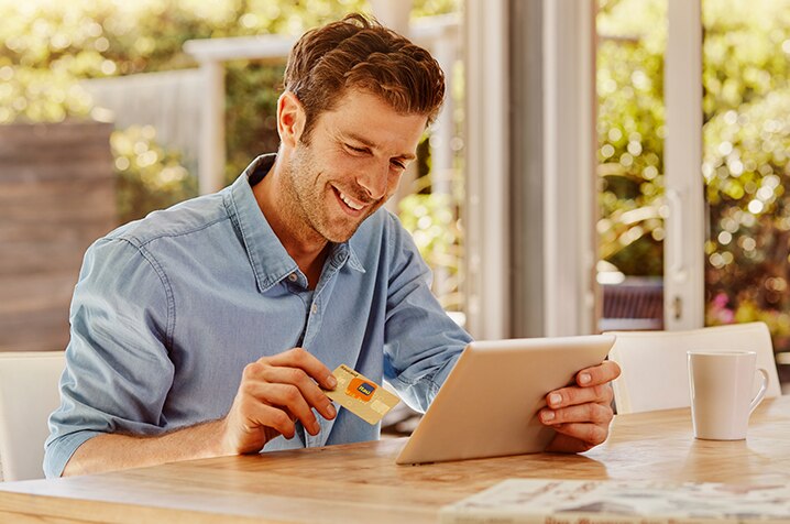 Cliente Itaú sorrindo segurando seu Itaucard na mão direita e um tablet na mão esquerda.