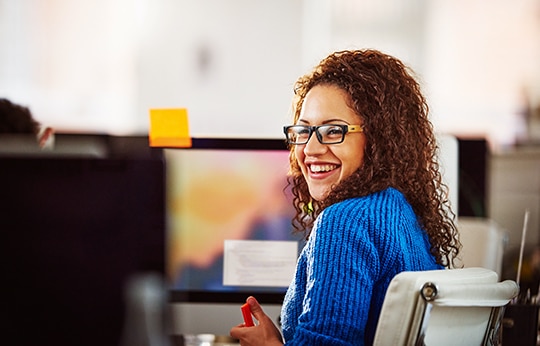 Cliente Itaú Empresas sorrindo e sentada em uma cadeira em um escritório.