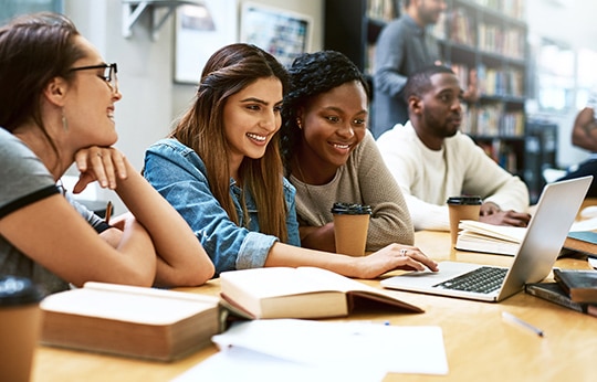Quatro estudantes felizes enquanto estudam em uma biblioteca.