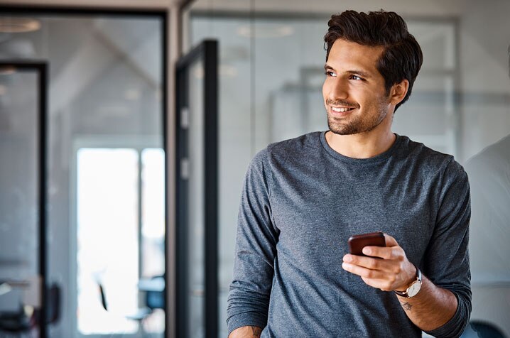 cliente Itaú sorrindo e segurando um Smartphone com a mão esquerda após fazer cadastro positivo. 