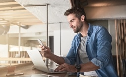 Homem cliente Itaú, em seu escritório, acessando sua conta-corrente pelo celular