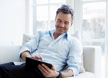 homem sorrindo sentado no sofá usando um tablet