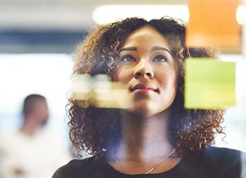 mulher olhando para uma parede de vidro com post-its colados