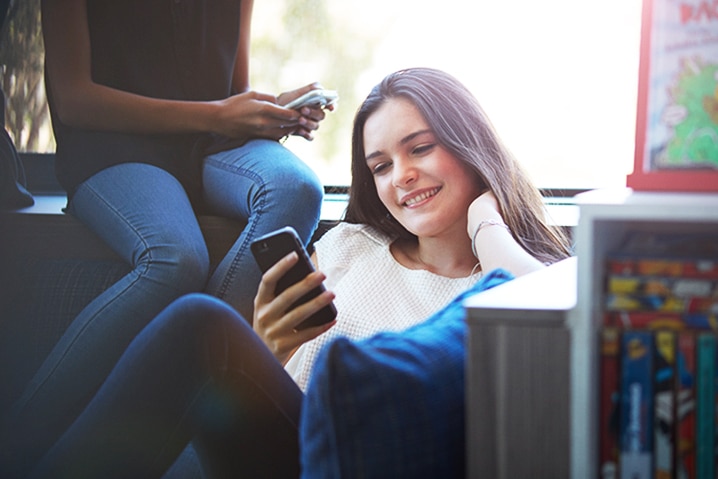 estudante usando o celular em um sofá em uma biblioteca.