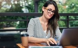 Mulher cliente Itaú, em uma varanda, tomando um café, solicitando um empréstimo pelo seu computador