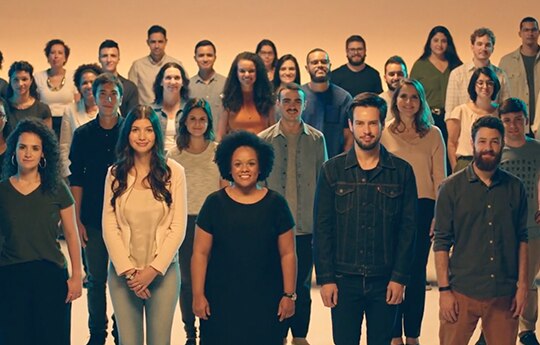 imagem com colaboradores Itaú em pé em um fundo laranja.