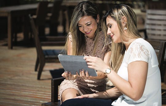 duas mulheres conversando e olhando para um tablet.