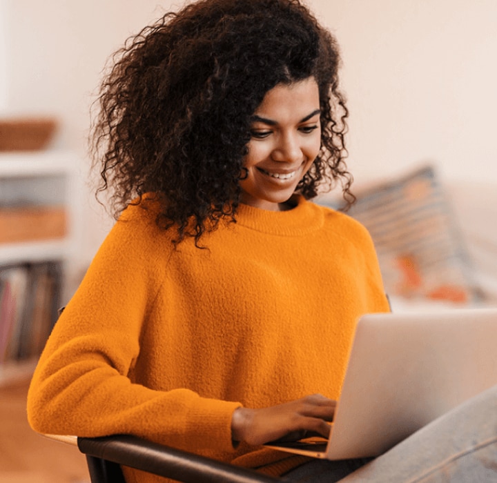 Mulher usando um suéter laranja, e olhando sorrindo para um notebook