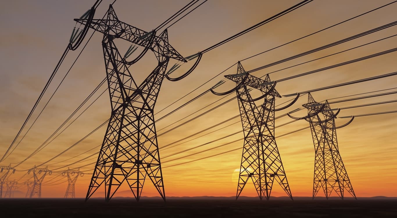 Torres de transmissão de energia elétrica sob um céu alaranjado ao pôr do sol, representando a infraestrutura de distribuição de energia.