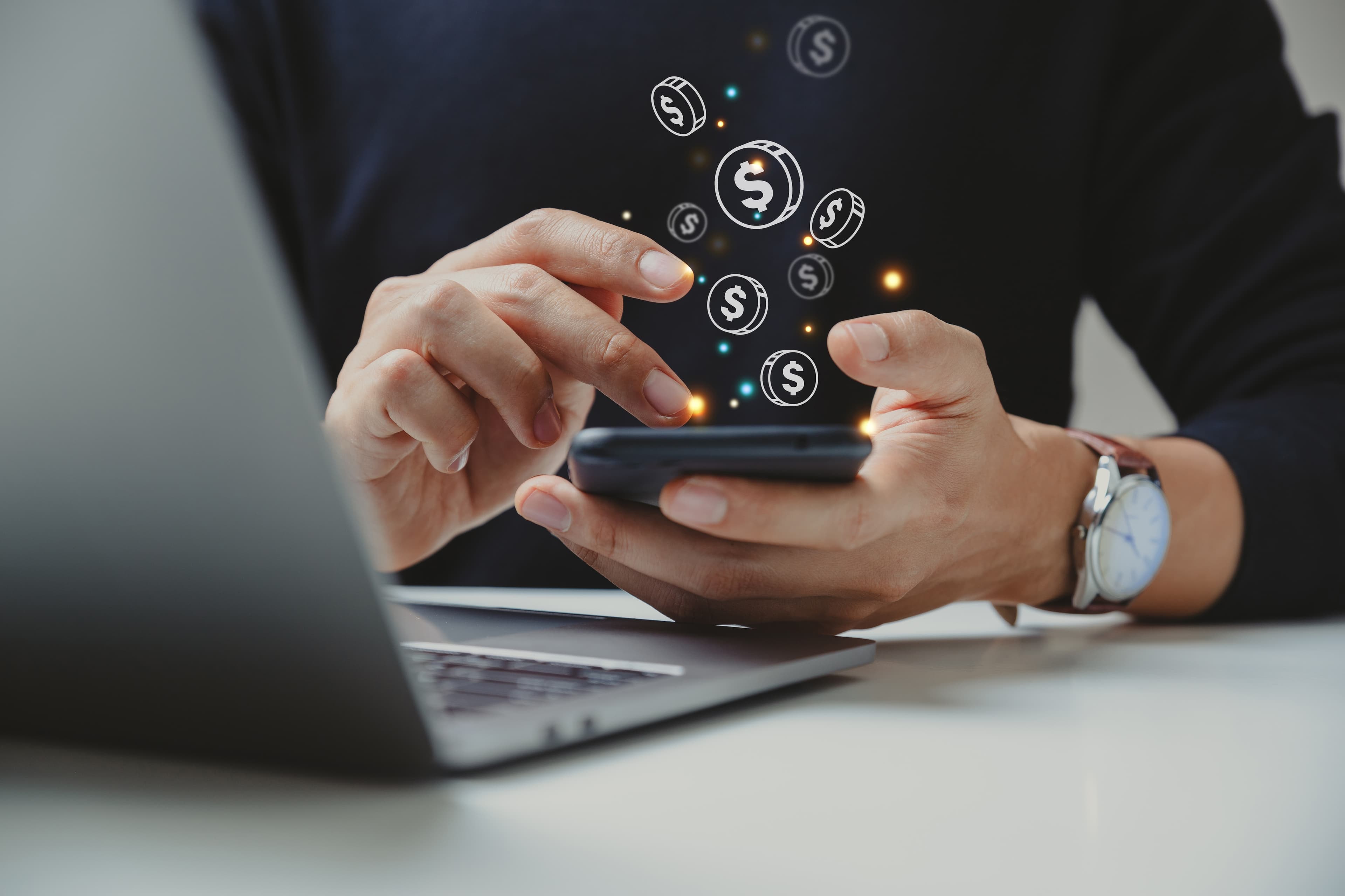 Imagem ilustrativa de um homem mexendo em um celular e símbolos de moedas "saindo" acima do telemóvel
