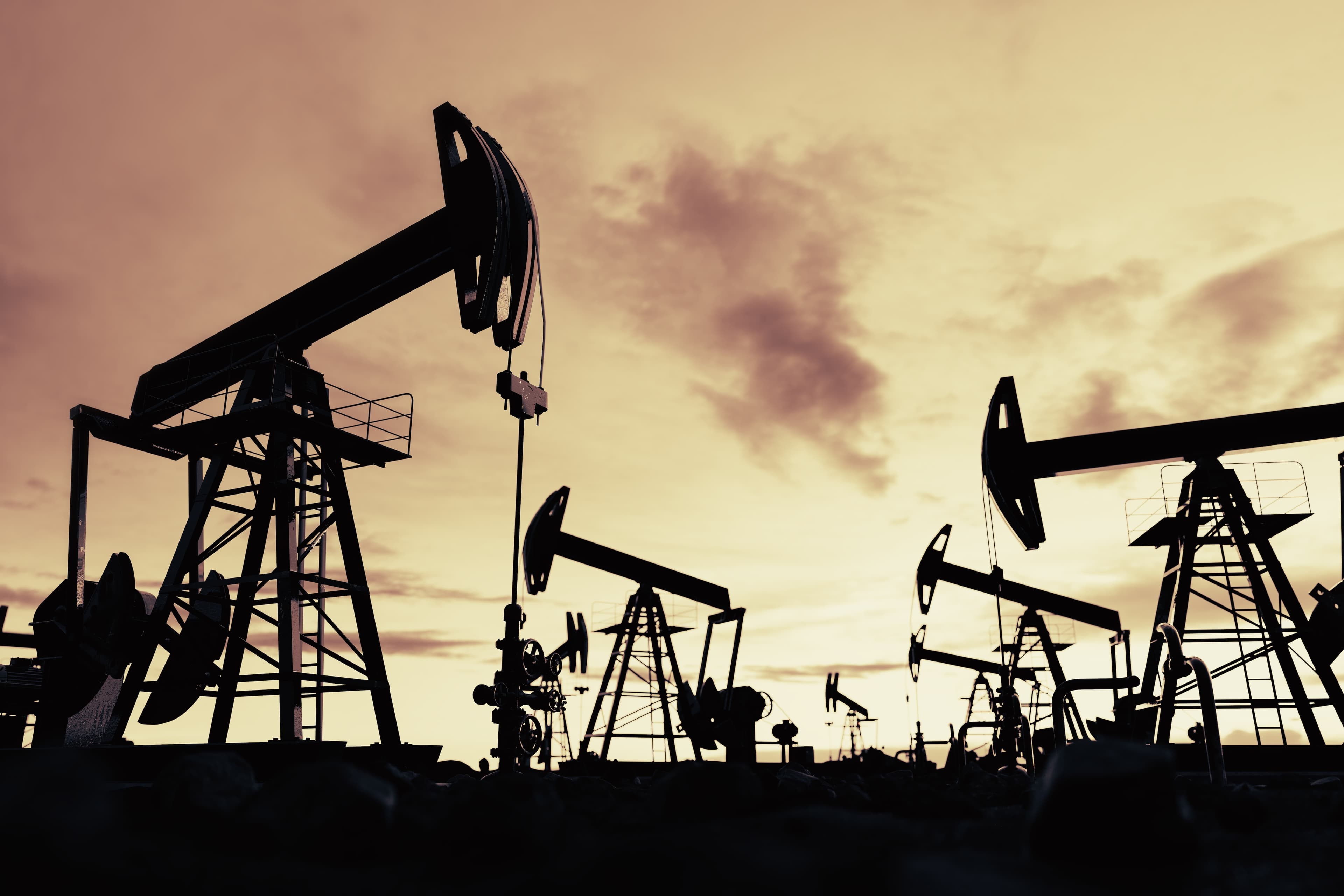 Bombas de extração de petróleo operando em um campo petrolífero ao entardecer.