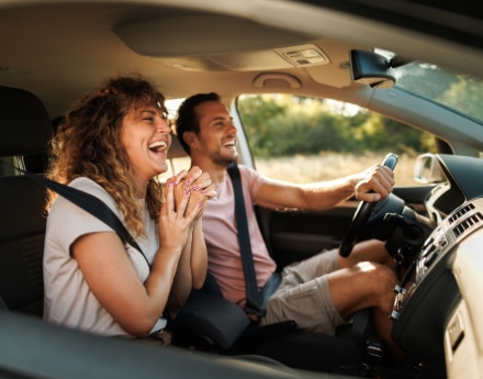 Imagem de um casal sorrindo dentro do automóvel.