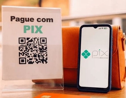 Escrito "Pague com Pix" acima de um QR code. Ao lado, um smartphone.