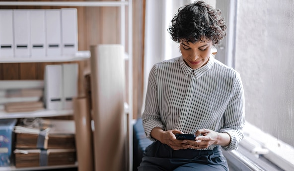 Pessoa sentada próxima à janela usando smartphone em escritório.