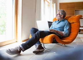Homem sentado em um sofá laranja e com um notebook no colo representando um novo cliente Itaú 