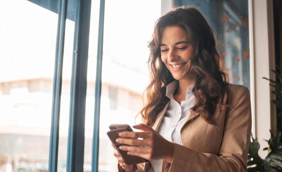 Mulher sorrindo enquanto acompanha pelo celular os investimentos da sua empresa