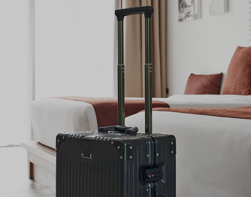 Imagem de uma mala de viagem em um quarto com duas camas ao fundo.