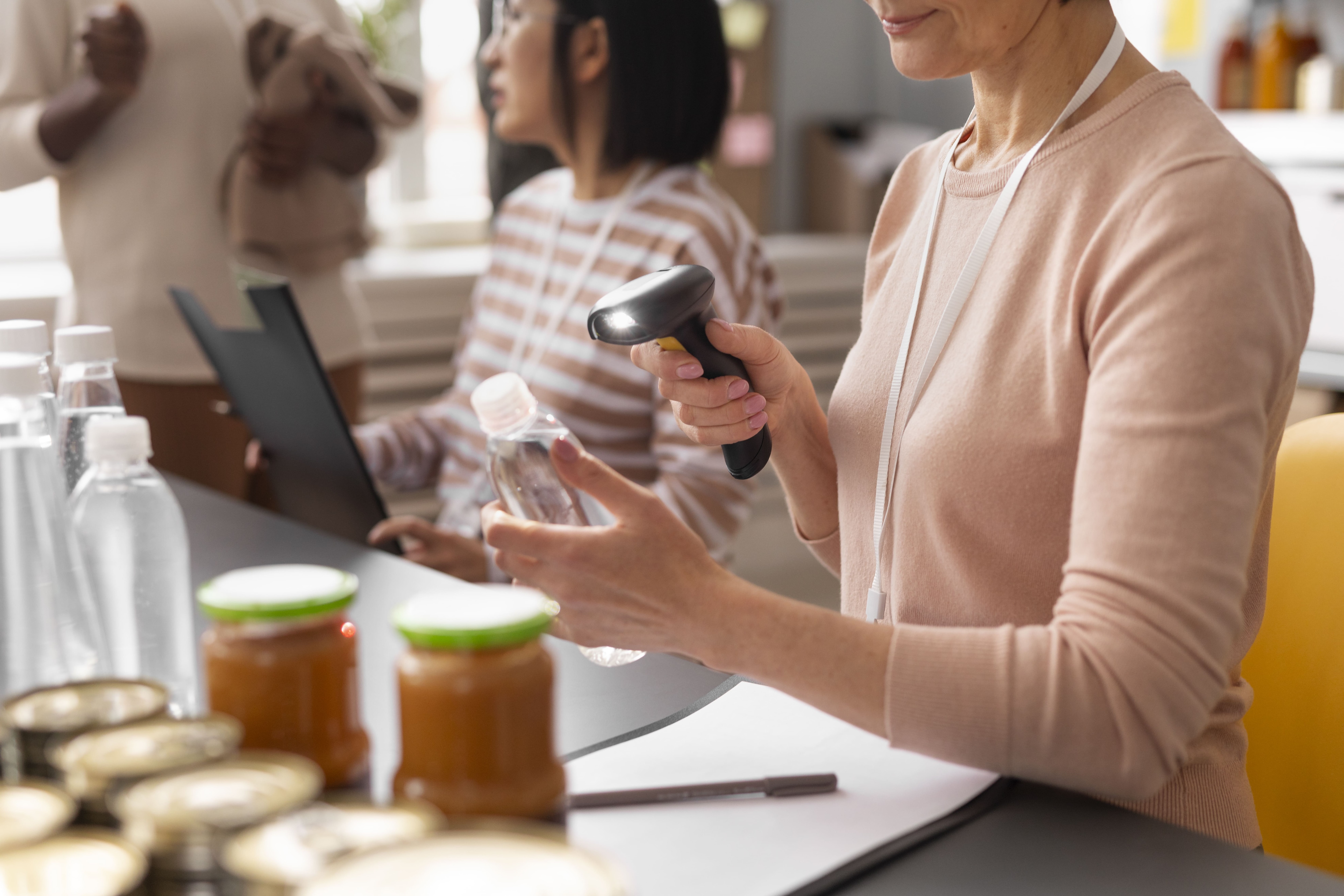 Na imagem há duas mulheres atrás de um balcão, com um leitor de código de barras, lendo o código de um produto
