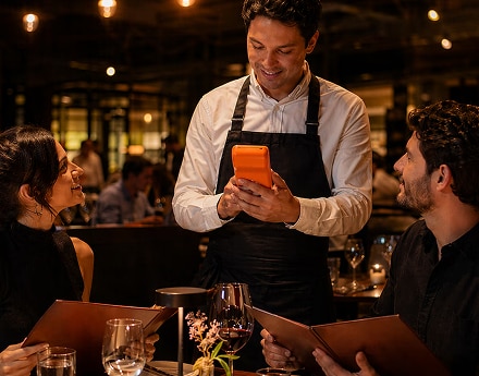 Pessoa com avental usa laranjinha para atender clientes à mesa.