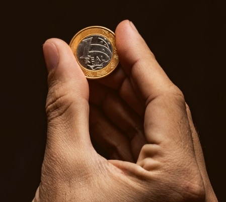 Mão segurando uma moeda de um real.