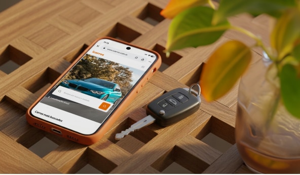 Celular e chave de veículo sobre mesa, com tela do app exibindo oferta de automóvel.