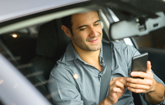 Homem dentro de um carro mexendo em seu celular