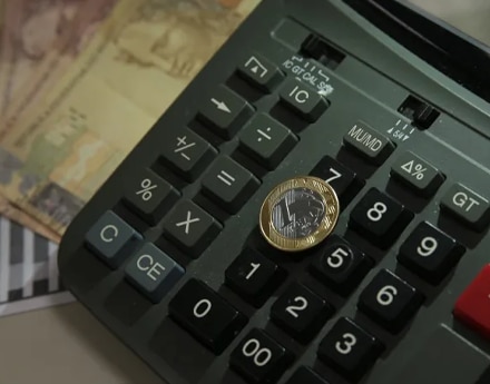 Imagem de uma calculadora e uma moeda de 1 real