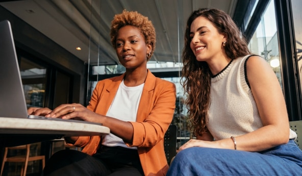 Duas mulheres sentadas na frente de um notebook, conhecendo o Mulher Empreendedora