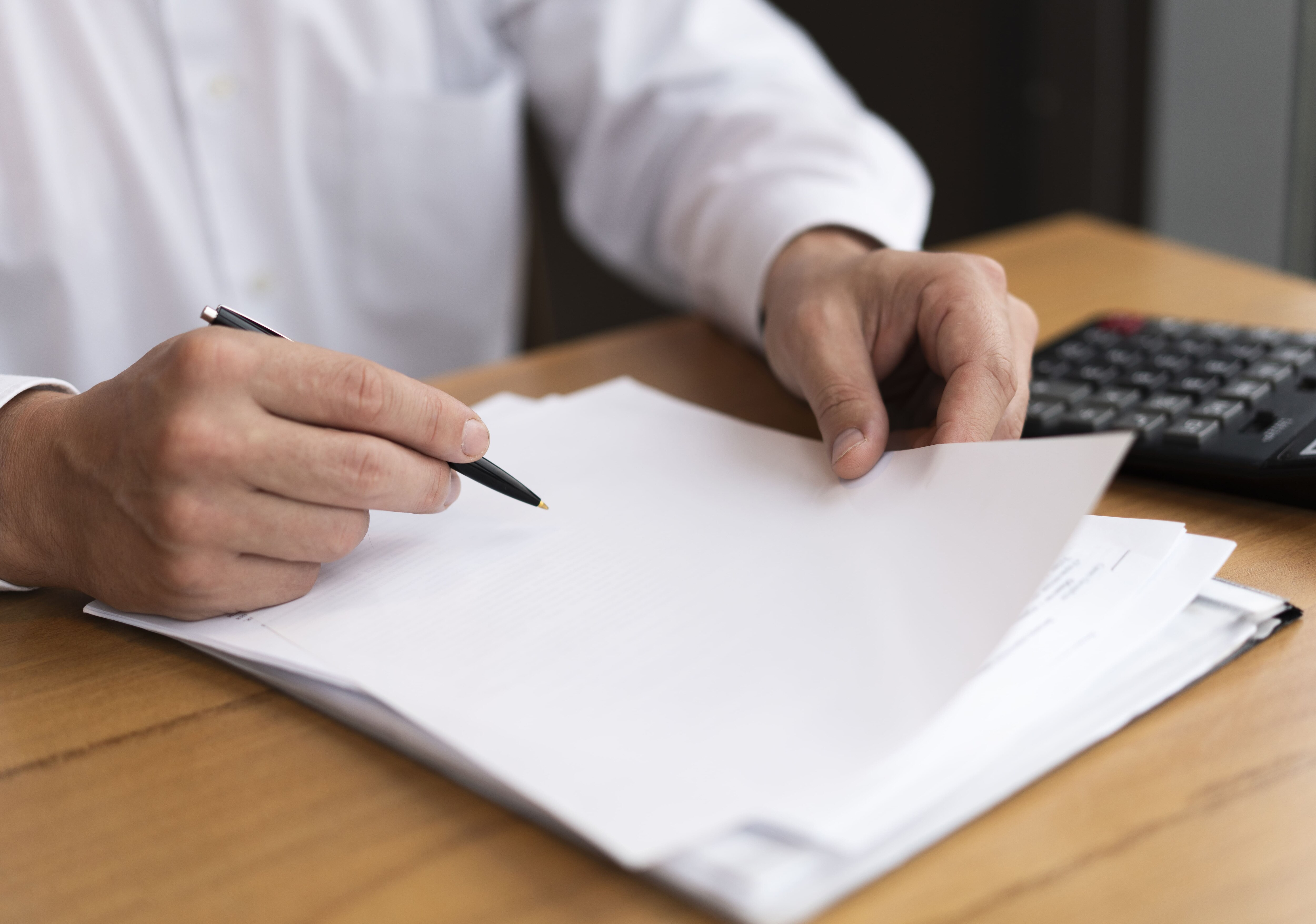 Imagem de uma mão de uma pessoa branca segurando um lápis preto, prestes a escrever em um papel em branco