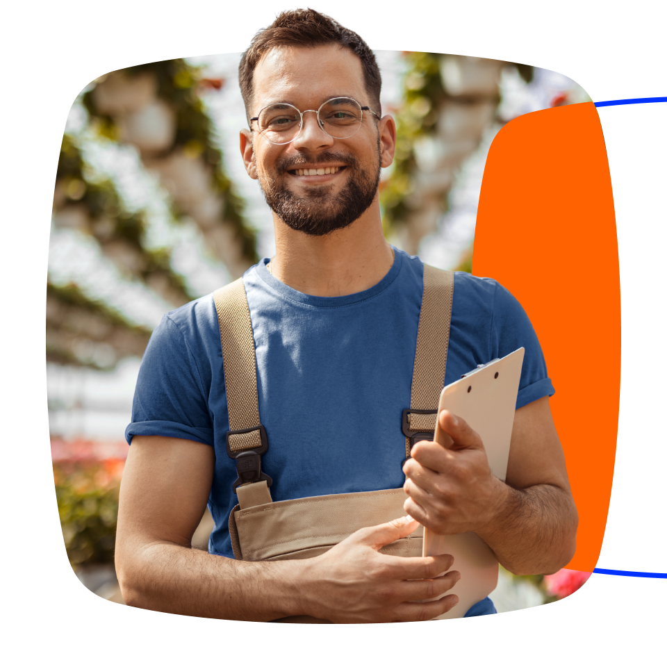 Homem jovem, pardo, usando óculos, empresário na agricultura, usando avental, sorrindo para a foto. Segura um tablet nas mãos.