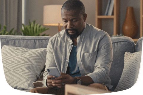 Homem negro sentado em um sofá, olhando para o celular.