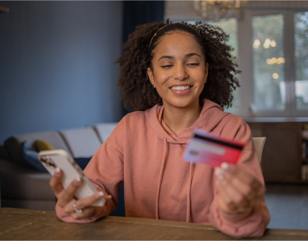 Mulher sorrindo enquanto segura um celular e um cartão nas mãos.