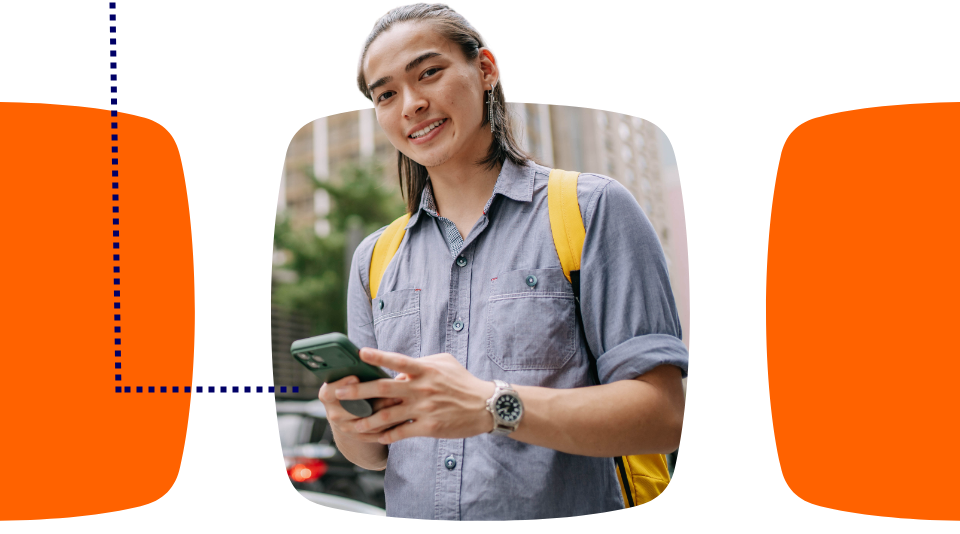 Homem mestiço, olhando para a câmera sorrindo, com o celular na mão.