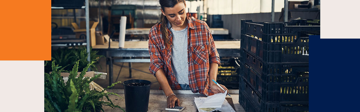 Mulher em um balcao fazendo contas com uma calculadora e papel na mao mobile