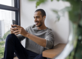 Homem utilizando um celular com fones no ouvido.