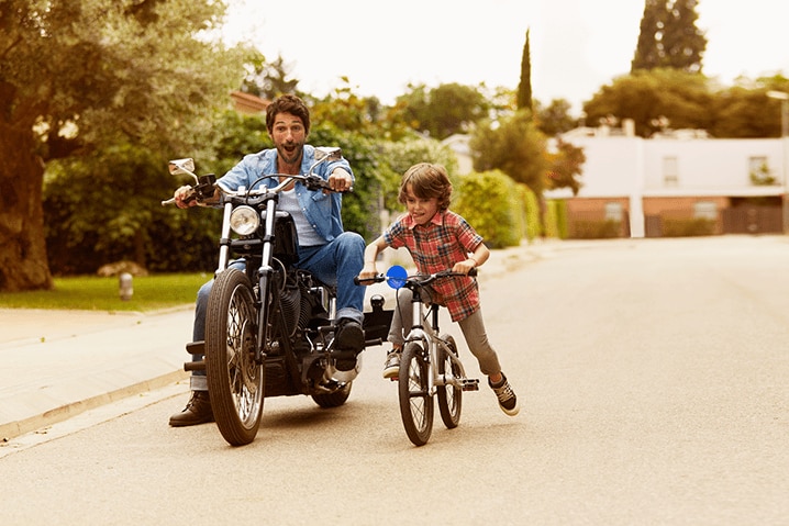 homem andando de moto ao lado do filho andando de bicicleta
