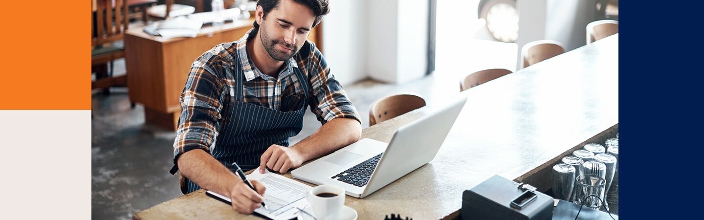 Homem fazendo anotações em frente a um notebook