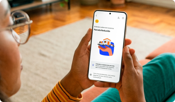 Cliente Itaú de óculos, com seu celular em mãos e o app aberta na tela de Consórcios com Parcela Reduzida.